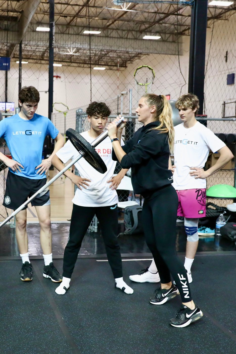Coach G demonstrating a barbell lift to three athletes